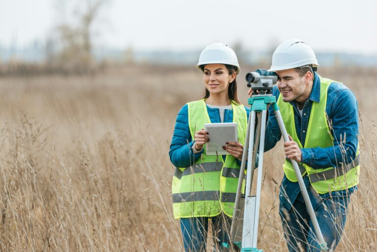 Smiling surveyors with digital level and tablet in field